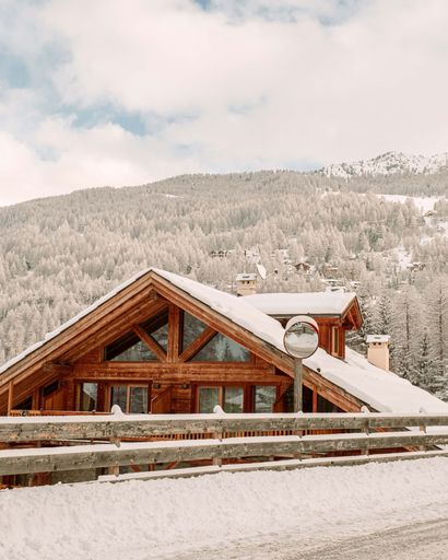 A modern wooden cottage with a snow-covered roof surrounded by a beautiful alpine scene