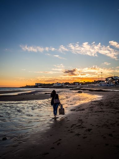 A vertical shot of a female walking through the beach at Carcavelos, Lisbon during the sunset