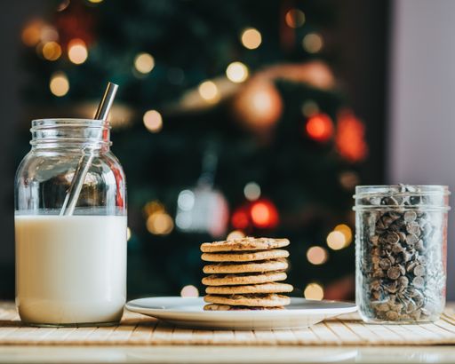 The chocolate chip cookies and a glass of milk with a Christmas tree in the background