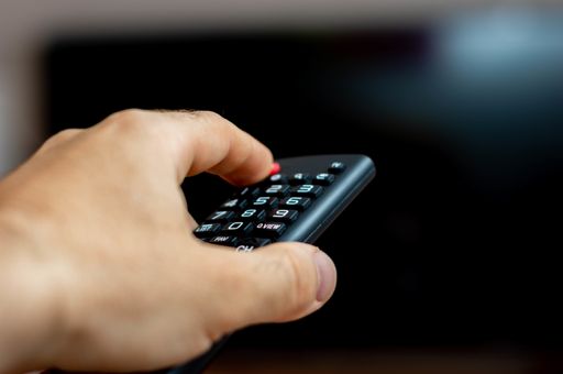 A male hand holding a TV remote and trying to turn on the TV