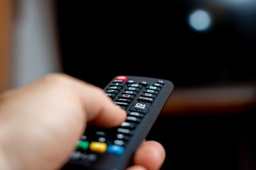 A male hand holding a TV remote and trying to turn on the TV