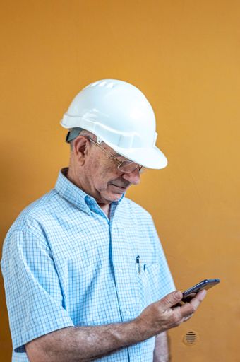 A vertical shot of a Caucasian engineer checking his mobile while wearing a safety helme