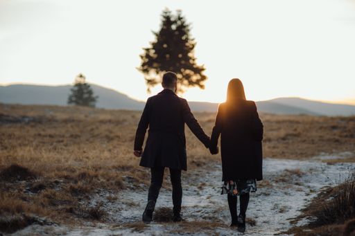 A shallow focus shot of a young couple walking through the field at the beautiful sunset