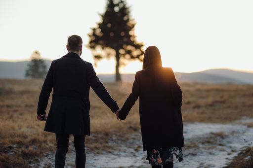 A shallow focus shot of a young couple walking through the field at the beautiful sunset