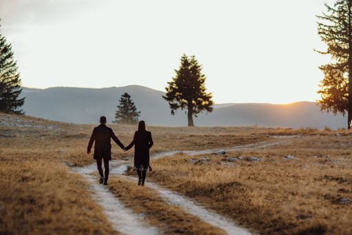 A shallow focus shot of a young couple walking through the field at the beautiful sunset