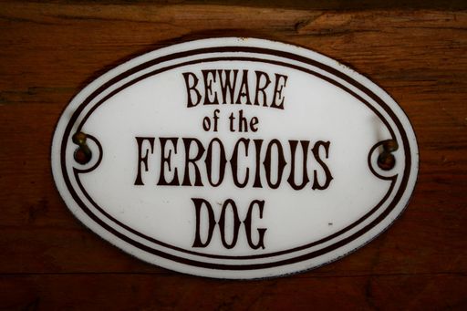 A "Beware of the ferocious dog" metal sign on wooden background