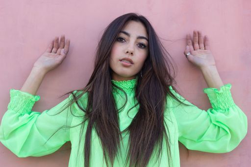 A beautiful young female wearing a green shirt and posing against a pink wall