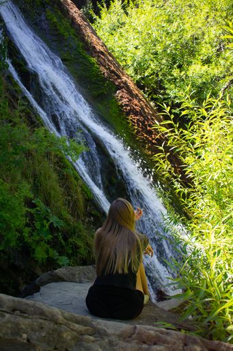 A vertical shot of a long-haired woman having a quiet time with nature beside a waterfall