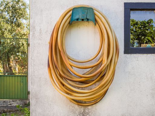 A long weathered garden hose hanging on a white wall during daytime