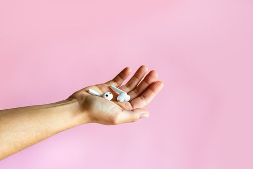 A closeup of a woman holding wireless earbuds in front of a pink background