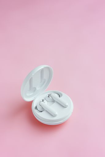A vertical shot of wireless earbuds in their case on a pink surface