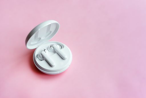 A closeup of wireless earbuds in their case on a pink surface