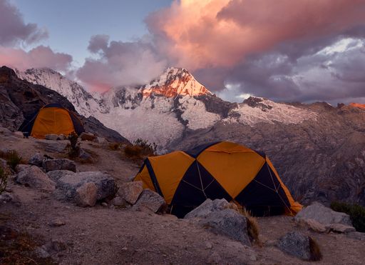 The camping tents on the rocks with the magical view of the mountains gleaming under the cloudy sky