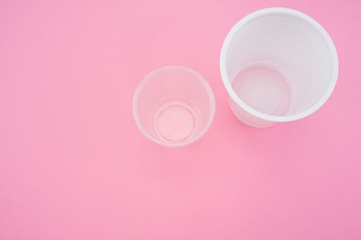 A high angle shot of big and small plastic cups on a pink surface
