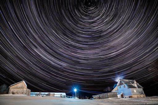 A landscape of wooden buildings and cottages covered in the snow under a starry sky with long exposure