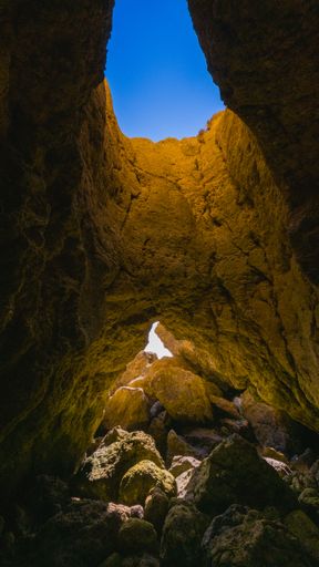 A low-angle view of an opening between the rocks with the blue sky visible from it