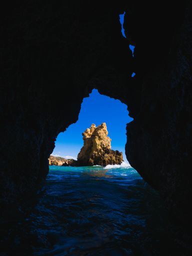 A scenic view of a coastal rock seen from a cave located on the shore of a beach