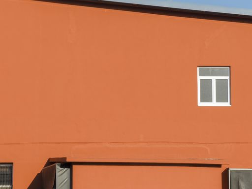 The orange exterior of a house with one small window, during daylight