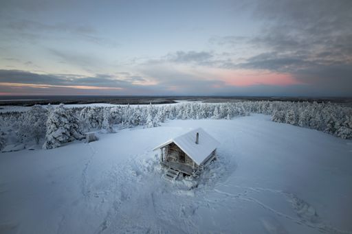 A high angle shot of an old cabin on a winter landscape with trees covered in snow during sunset