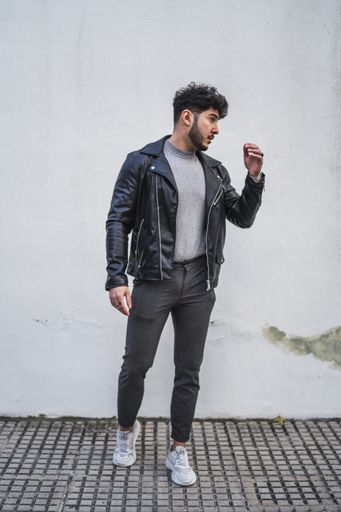 A vertical shot of a handsome European male in a black leather jacket posing against a white wall