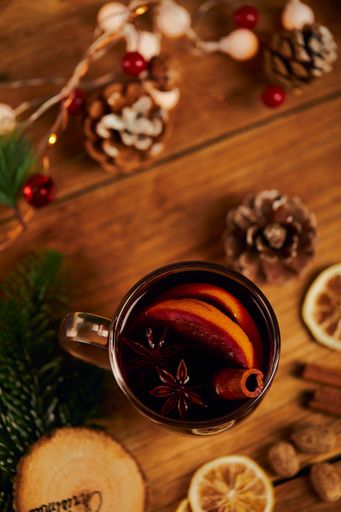 A cup of hot tea with citrus and cinnamon on wooden table with dried lemon slices and Christmas decors