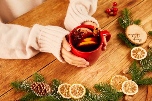 A top view of female hands holding a red mug of hot tea with citrus and cinnamon on wooden table