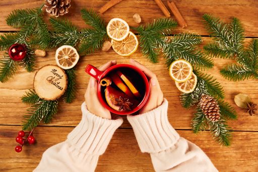 A top view of female hands holding a red mug of hot tea with citrus and cinnamon on wooden table