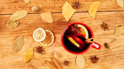 A top view of a mug of mulled wine with cinnamon sticks and orange on a wooden table