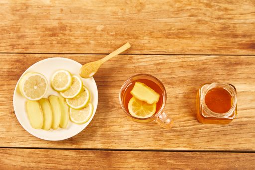 A top view of cup of tea with lemon, ginger and honey, jar of honey and plate with ginger and lemon