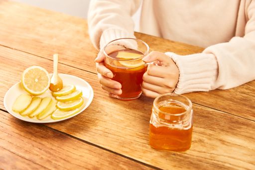 A female holding a cup of hot tea with honey, lemon and ginger - home treatment