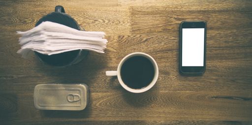 A top view of a coffee mug near a smartphone on a wooden table