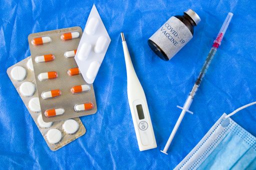 A top view of the COVID-19 vaccine with facemask, drugs, and a thermostat on a blue surface