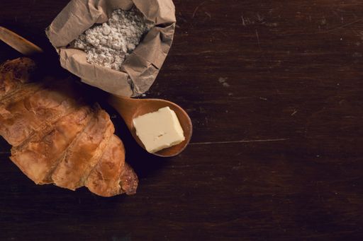 An overhead shot of croissants on a wooden table with butter and a flour bag