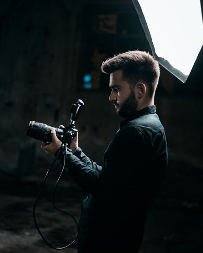 A shallow focus of an adult cameraman filming in a studio with a dark blurry background