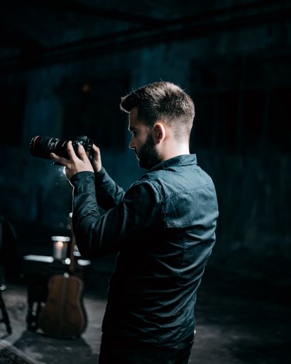 A shallow focus of an adult cameraman filming in a studio with a dark blurry background