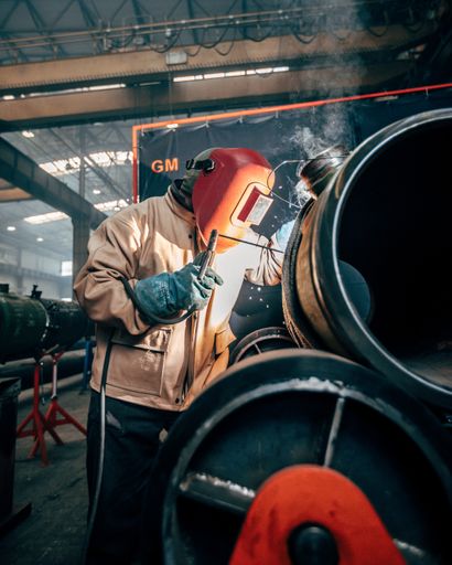 A vertical shot of a welder wearing a helmet and welding steel tubes in a factor