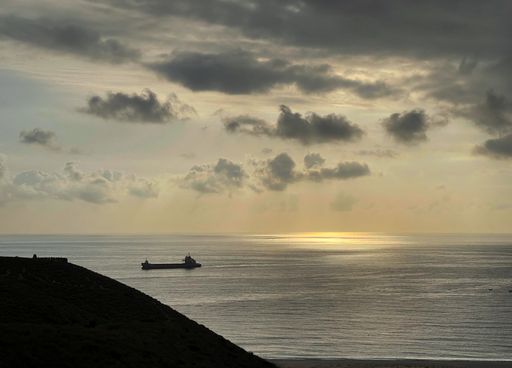 A ship passing on calm sea surface during a mild sunset with cloudscape in the background