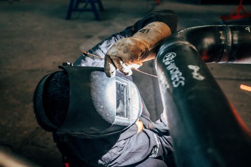The worker with protective equipment welding pipe in manufacturing plant