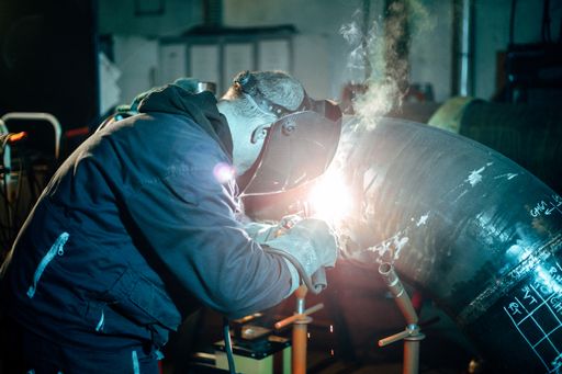 The worker with protective equipment welding pipe in manufacturing plant