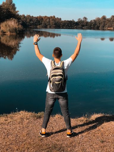 A back view of a young male standing with hands up and looking at the lake