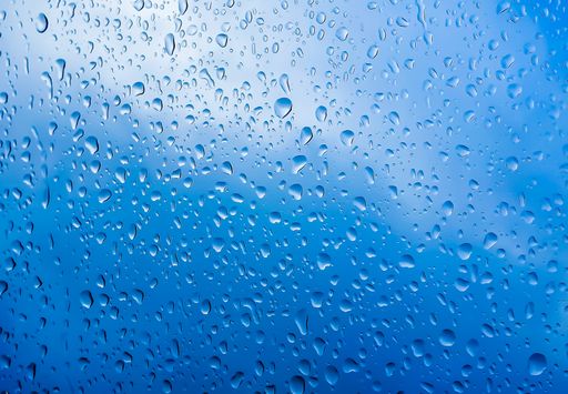 A closeup shot of raindrops running down a window against a blue background