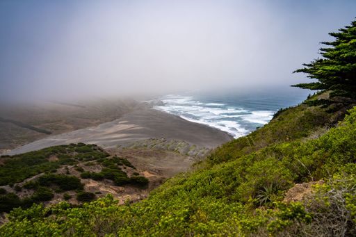 A scenic view of the vast expanse of the ocean from the edge of a cliff, with a rocky outcropping providing a stunning natural overlook