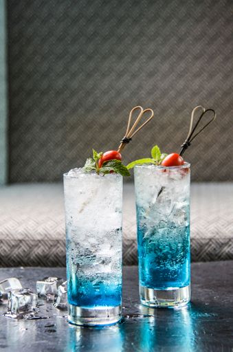 A vertical shot of two glasses of blue cocktail with garnish on the bar