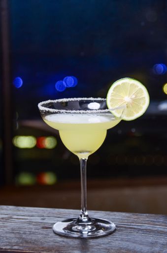 A vertical shot of a glass of margarita with a slice of lime on the bar