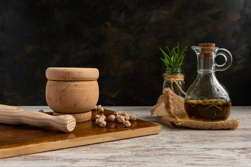 A closeup of chickpeas in a wooden mortar and pestle, next to an olive oil bottle, on a wooden surface