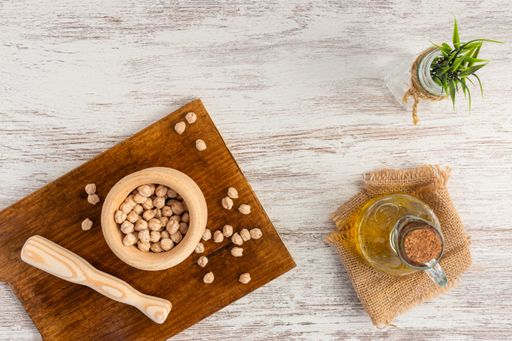 A top vi of chickpeas in a wooden mortar and pestle, next to an olive oil bottle, on a wooden surface