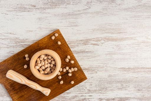 A top view of chickpeas in a wooden mortar and pestle, on a board, placed on a wooden surface