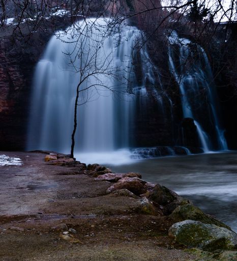 A closeup shot of a waterfall in rocks surrounded by bare trees on an autumn day