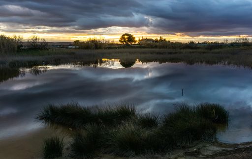 A closeup shot of a storm over a rural house in the countryside near a reflecting lake