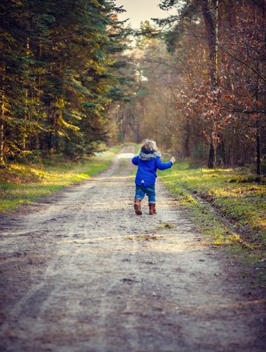A vertical shot of a caucasian blond boy running on a trail surrounded by a forest